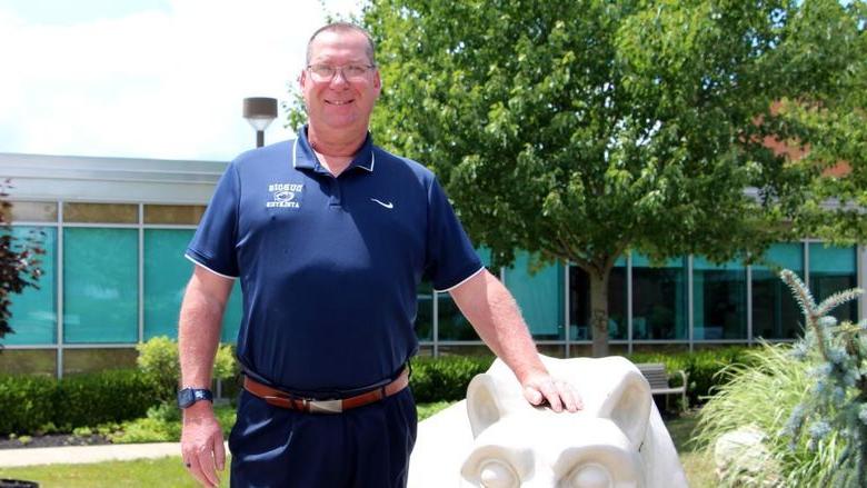 New head golf coach at Penn State DuBois John Schneider stands with the Lion Shrine on campus.